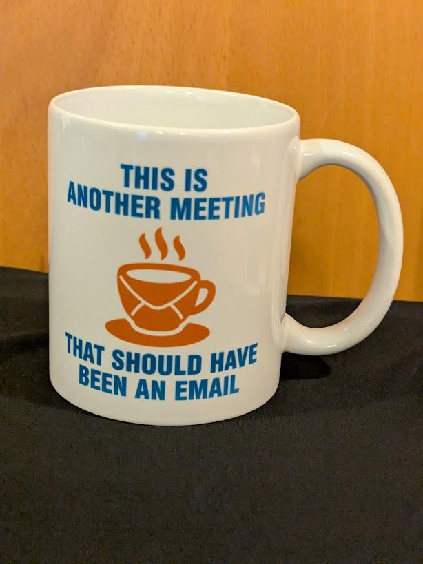 White mug with blue writing: This Is Another Meeting That Should Have Been An Email. A orange coffee mug icon is in the middle.